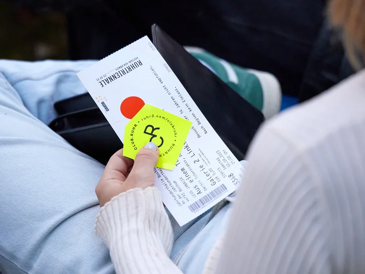 Eine Person hält ein Veranstaltungsticket auf ihrem Schoß fest.