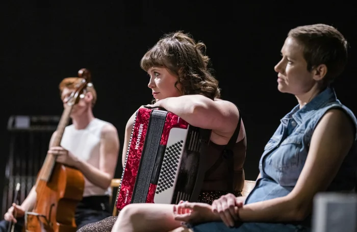 Jacob Garside, Sally Swanson, Meriel Price auf der Bühne sitzend mit Instrumenten