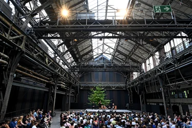 Jahrhunderthalle Bochum: Blick auf die Bühne der Veranstaltung "Brave New Voices". Es sind die Moderatorin Fatima Khan und der Schriftsteller Édouard Louis zu sehen. Im Vordergrund sieht man das Publikum.