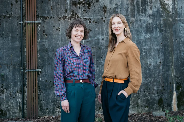 Colleagues Stefanie Matjeka and Stefanie Noack from the Ruhrtriennale press office stand in front of a wall and smile at the camera.