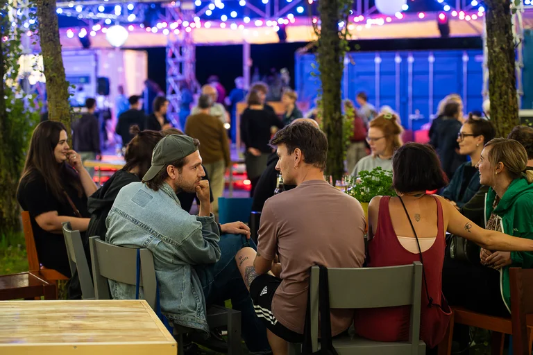 Junge Menschen sitzen bei Nacht in der Pappelwaldkantine der Ruhrtriennale, beleuchtet von Lichterketten