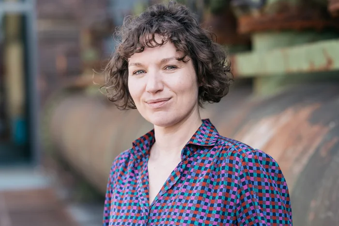 Stefanie Matjeka stands in front of a rusty machine and looks into the camera.