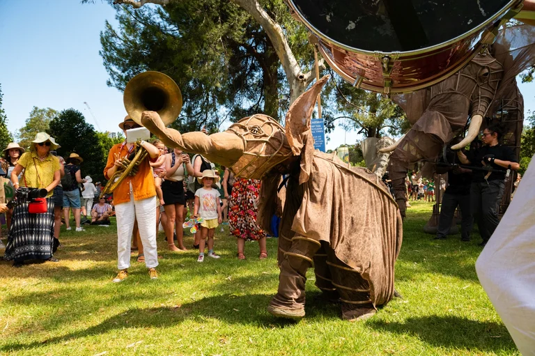 Lebensgroße Elefantenfiguren umgeben von Personen mit Instrumenten und Kindern