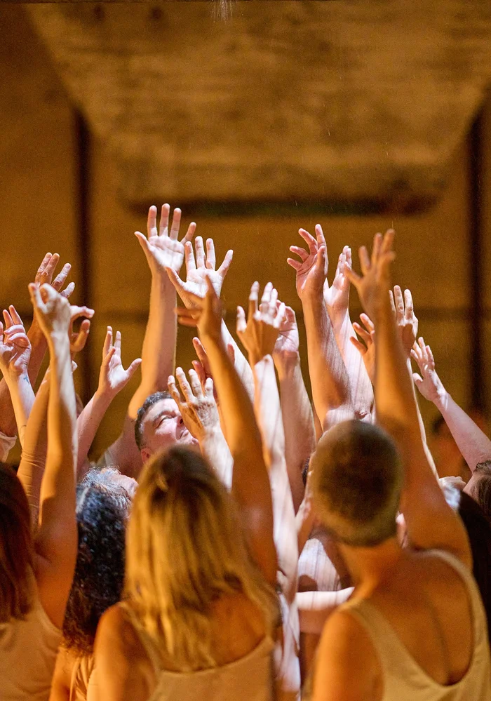 A group of people stretch their hands towards a funnel in a concrete ceiling.